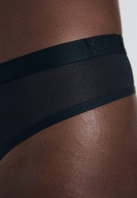 Cueca preta transparente com uma textura suave e uma cintura elástica estreita. O tecido parece leve e semi-transparente.