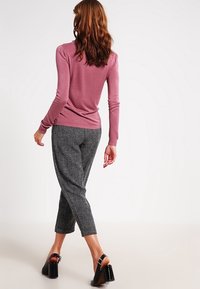Dopasowany różowy sweter z długim rękawem połączony z teksturowanymi czarno-białymi spodniami w kratę houndstooth do kostek i czarnymi sandałami na obcasie.