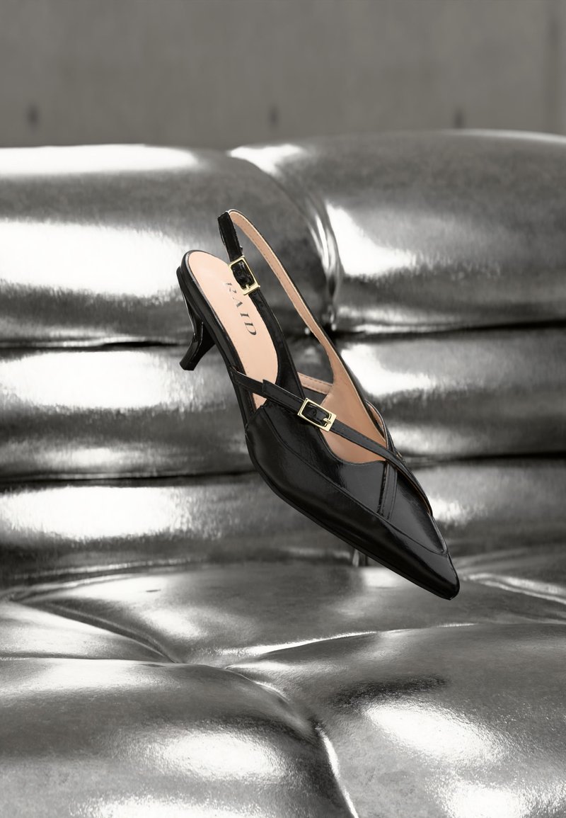 Escarpin slingback à petit talon en cuir verni noir avec boucle dorée reposant sur un revêtement en cuir argenté capitonné et brillant.