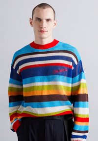Pull en tricot avec des rayures horizontales vibrantes dans les tons de bleu, rouge, marron, orange et vert, avec une finition texturée et un col rouge.