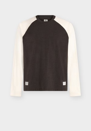 Ilgomis rankovėmis raglano marškinėliai su juodu liemeniu ir baltais rankovėmis, apvaliu kaklu ir mažomis BDG prekės ženklo etiketėmis apačioje priekyje.