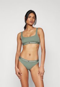 Zelená elastická podprsenka a bikiny s čtvercovým výstřihem a širokými ramínky, s logovou páskou s nápisem "TOMMY HILFIGER" v bílé barvě.