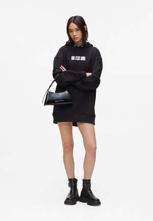 Black oversized hoodie with a front graphic, paired with a black patent leather mini bag and chunky black ankle boots.