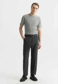 Szary prążkowany sweter z krótkim rękawem, w połączeniu z ciemnymi spodniami w pionowe paski i czarnymi sznurowanymi butami, z czarnym paskiem ze srebrną klamrą.