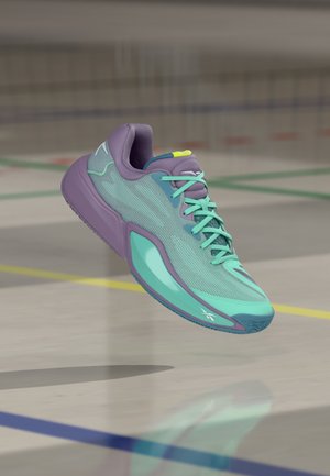 Chaussure de sport violette et bleu sarcelle avec des lacets vert menthe flottant au-dessus d'un sol de terrain intérieur poli avec des lignes colorées.