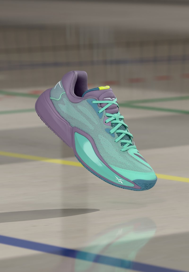 Fioletowo-turkusowy but sportowy z miętowozielonymi sznurowadłami unoszący się nad polerowaną podłogą hali sportowej z kolorowymi liniami.
