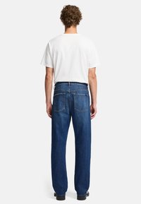 Donkerblauwe spijkerbroek met een rechte pijp, voorzien van twee achterzakken en een gestikte tailleband, gecombineerd met een eenvoudige witte T-shirt.
