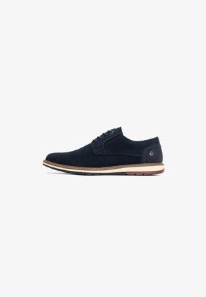 Zapato de ante azul marino con una suela intermedia de color marrón claro, diseño de cordones, puntera redonda y mínimas acentuaciones rojas cerca de los ojales y en el lateral.
