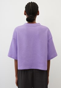 Lyhythihainen, cropped lila paita, joka on valmistettu tekstuurikankaasta, jossa on kauluspääntie ja rento istuvuus. Yhdistetty tummaan, väljään housuun.