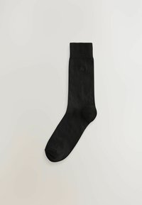 Schwarze Socke aus einem glatten, leichten Stoff. Verfügt über einen gerippten Bund und eine verstärkte Zehenpartie. Keine sichtbaren Muster oder Beschläge.