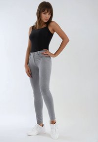 Body negro sin mangas combinado con leggings ajustados grises, con textura suave y cierre de dos botones, complementado con zapatillas blancas.