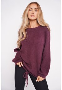 Burgundowy, oversize sweter z miękkiego, puszystego materiału, z okrągłym dekoltem, długimi rękawami i regulowanym dnem na sznurki. W połączeniu z czarnymi legginsami.