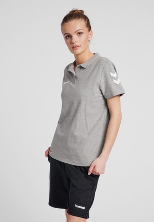 Grå polo shirt med krave og korte ærmer, med et hvidt logo og chevron-design på venstre ærme. Kombinationen med sorte shorts.