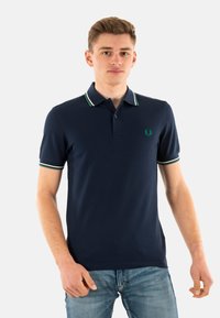 Polo navy hecho de una mezcla de algodón, con un cuello clásico, tapeta de dos botones y puños a rayas verdes y blancas en contraste.