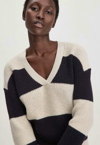 Strickpullover mit V-Ausschnitt, lässiger Passform, abwechselnd schwarzen und beigen Streifen, strukturiertem Stoff und gerippten Bündchen.