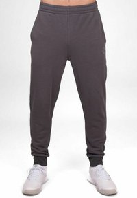 Pantalons de survêtement gris avec un design effilé, ceinture élastique et poignets côtelés. Présente un logo discret sur le côté et un tissu doux et texturé.