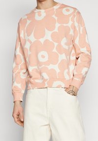 Felpa rosa chiaro con grandi motivi floreali bianchi, scollo rotondo, polsini e orlo a coste. Realizzata in tessuto morbido, presenta una vestibilità comoda.