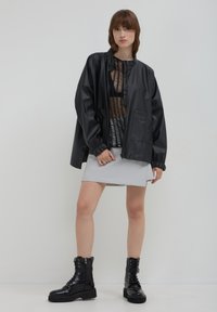 Giacca nera, lucida e oversize con zip frontale e polsini elasticizzati, abbinata a una mini gonna grigia chiara e stivali da combattimento neri con lacci.