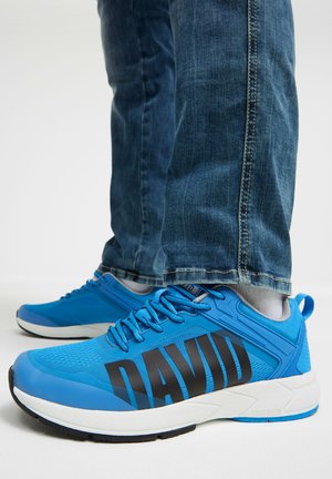 Blue athletic shoes with black "DAVID" text on the sides, worn with light gray socks and blue denim jeans.