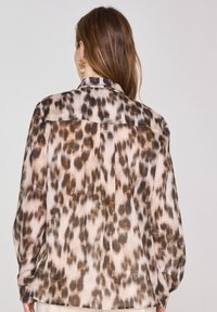 Camicia a fantasia leopardata in beige e marrone, realizzata in tessuto leggero. Presenta un colletto, maniche lunghe e un design con yoke sul retro.