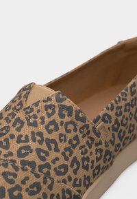 Παπούτσι τύπου slip-on με καφέ και μαύρο ύφασμα λεοπάρ, ελαστική ένθετη λωρίδα για εφαρμογή και μπεζ σόλα, γωνιακό για να φαίνονται οι λεπτομέρειες από πάνω και πλάγια.