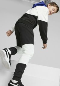 Schwarz-weißer color-blocked Trainingsanzug mit Kapuze in Blau. Die Jogginghose hat eine gerippte Textur und elastische Bündchen, kombiniert mit schwarzen Sneakers.