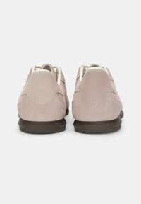 Chaussures en daim rose clair avec une finition texturée, de forme arrondie et des semelles en caoutchouc foncé. Présentent des coutures décoratives sur le talon.