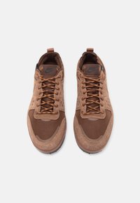 Scarpe da ginnastica marroni realizzate con una combinazione di materiali in suede e mesh, dotate di lacci marroni, una protezione rinforzata sulla punta e una suola testurizzata.