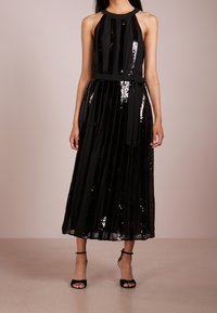 Musta helmikiristys halterneck-mekko, jossa on istuva bodice ja virtaava laskostettu hame. Mukana on yhteensopiva kangasvyö. Avoimet mustat korkokengät.