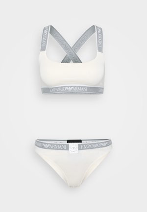Top sportivo bianco e bikini abbinato con elastici grigi che presentano il logo "Emporio Armani". Tessuto liscio con spalline incrociate.