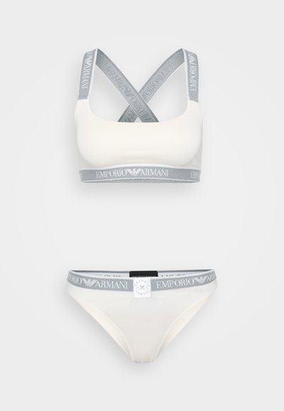 White sports bra and matching bikini with grey elastic bands featuring "Emporio Armani" logo. Smooth fabric with crisscross straps.