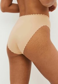 Slips beige a vita alta con bordo scallop, realizzati in materiale liscio e leggero, che presentano un design senza cuciture e una consistenza morbida.