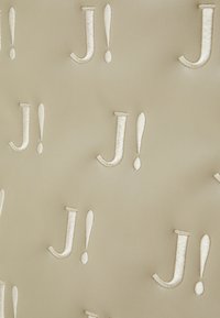 Tissu beige texturé présentant des "J!" en relief de couleur crème et des points d'exclamation dans un motif répétitif. Détail de surface lisse et doux.