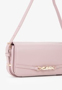 Bolso de mano de piel rosa con textura suave, detalles en hardware dorado y una delgada correa para el hombro. Presenta un acento trenzado cerca del cierre.