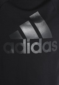 Czarna bluza z dużym, błyszczącym czarnym logo Adidas na piersi, o gładkiej fakturze i okrągłym dekolcie.