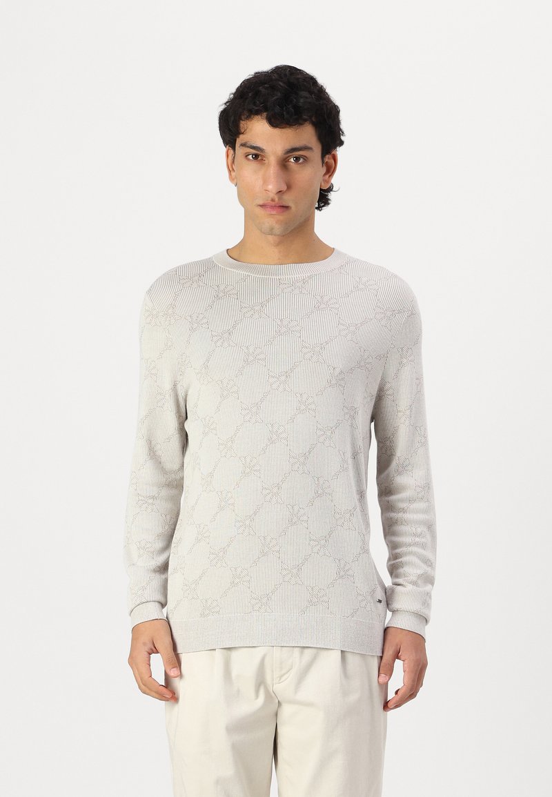 Suéter de punto gris claro con un patrón texturizado, cuello redondo y mangas largas, combinado con pantalones de color claro.