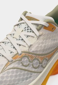 Αθλητικό παπούτσι σε ανοιχτό μπεζ και πορτοκαλί χρώμα με επάνω μέρος από δίχτυ, λευκά κορδόνια που σταυρώνονται και επενδυμένο πάτο με πορτοκαλί λεπτομέρεια.