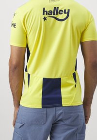 Gelbes Sportshirt mit dunkelblauen Streifen an den Seiten und am Rücken, mit dem Markennamen "halley" und einem Sternen-Graphic. Design mit kurzen Ärmeln.