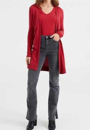Long cardigans rouges avec des poignets côtelés, porté sur un top rouge à col en V, associé à un jean gris foncé taille haute et des bottines à talons noires.