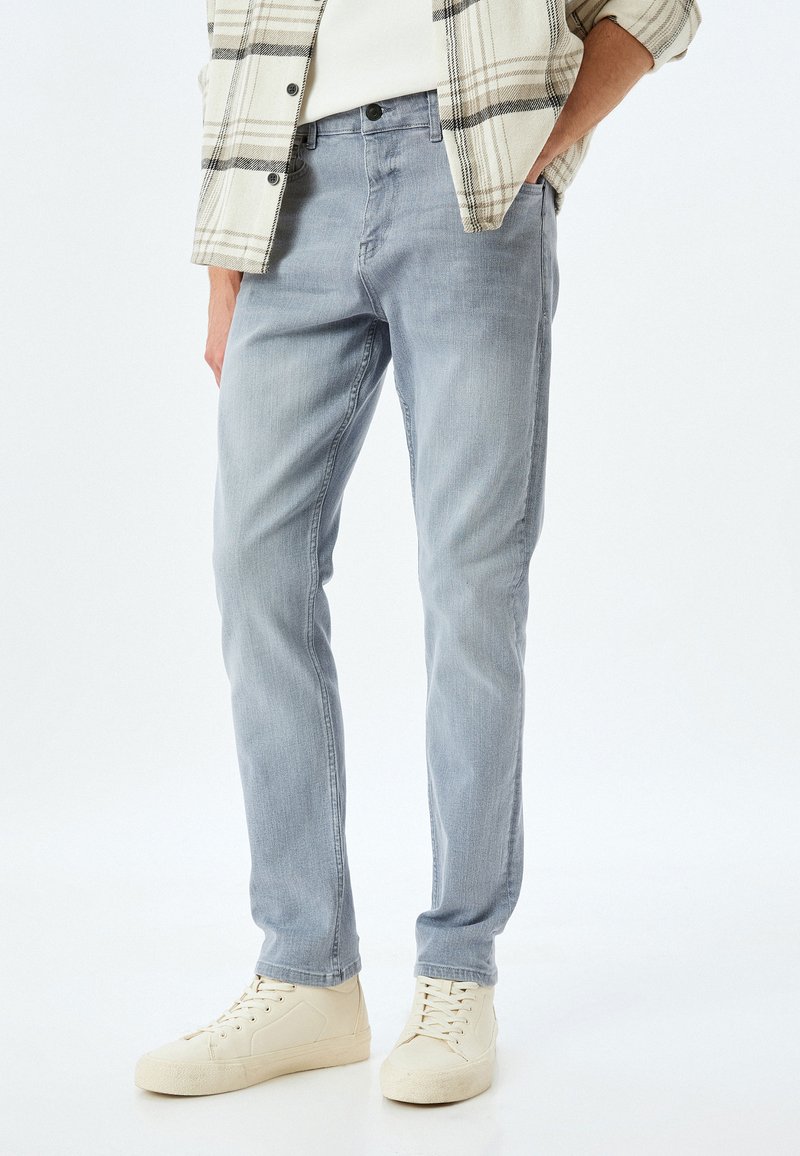 Jeans de mezclilla azul claro con un corte ajustado, que presentan un desgastado sutil y un diseño de cinco bolsillos, combinados con zapatillas de deporte beige.
