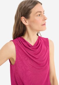 Fuchsiová bezrukávová halenka s krkem ve tvaru koryta, jemnou texturou a jemným žebrováním. Má uvolněný střih a otevřené průramky.