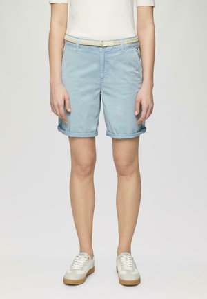 Shorts bleu clair en coton avec des ourlets retournés, dotés de poches latérales et d'une ceinture tressée beige. Portés avec des sneakers blanches et beiges.