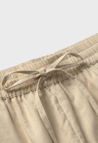 Beige elastische taillebroek met een trekkoord. Zachte, gestructureerde stof met een verticale ribbelontwerp langs de tailleband.