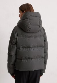 Donkergrijze gewatteerde jas met een hoge kraag en horizontale stiksels. De buitenkant is soepel met een matte afwerking. Met een capuchon.