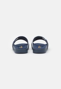 Navy flip-flops with dual straps and textured textile upper, featuring a flat rubber sole and gold logo detail on the insole.