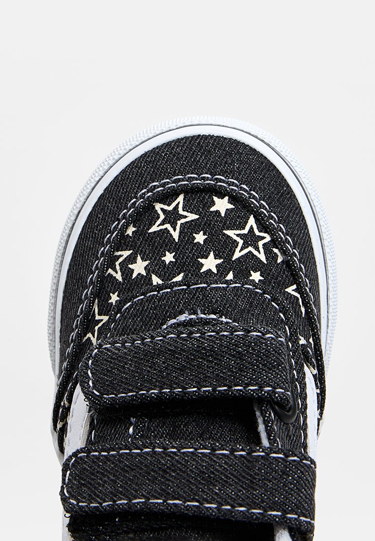 Zapato de mezclilla negra con patrón de estrellas blancas, correas de Velcro y suela blanca. Presenta costuras en contraste y tela texturizada.
