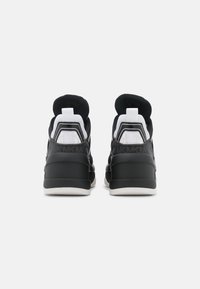 Černobílé sportovní boty s texturovaným svrškem, polstrovaným límcem a silnou gumovou podrážkou, se zvýrazněním paty v kontrastní barvě.