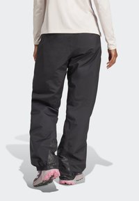 Sorte udendørsbukser med elastiske manchetter og en struktureret sort detalje ved anklerne, parret med lyst fodtøj.