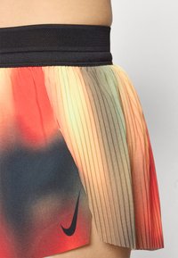 Nike plisserte skjørt har en svart elastisk midjebånd, gradient fargemønster med røde, oransje og grønne nyanser, samt en svart logoakcent.