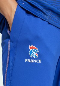 Plave atletske kratke hlače s teksturiranim materijalom, s logotipom pijetla u crvenoj, bijeloj i plavoj boji, te riječju "FRANCUSKA" ispod logotipa.